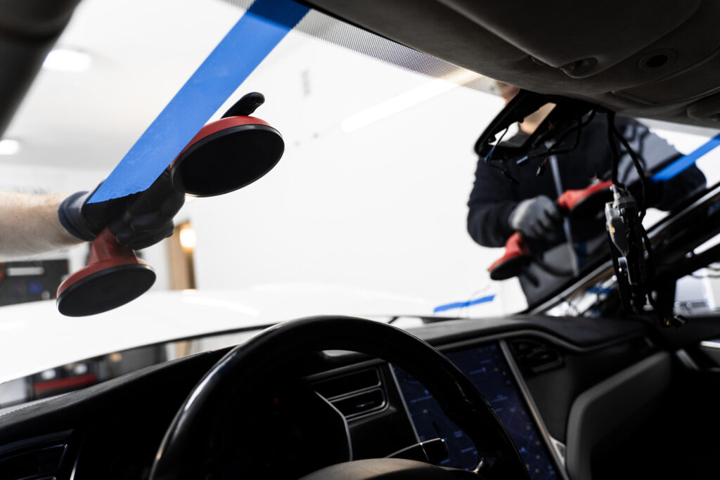 Technician installing a windshield using suction tools inside a modern vehicle during auto glass replacement service